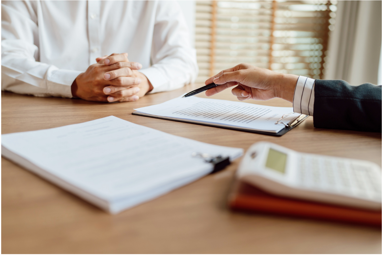 Photo of a desk with two people sitting across from each other, documents on the table.